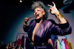 A woman in a purple power suit biting a chain. Karyn Rudance Creative Director