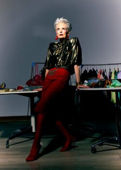 A woman in a power suit leaning against a table with fashion accessories. Karyn Rudance Creative Director