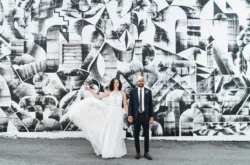 hair styling for wedding - bride with dark curly hair standing with groom in front of a black and white graffiti wall.