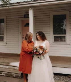 hair styling for wedding - bride with shoulder length curly hair standing with mom holding a bouquet.