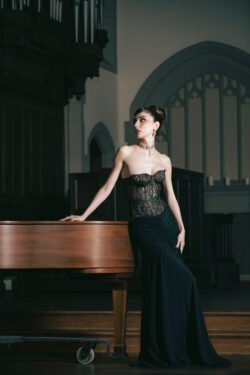 Editorial Photography - model leaning on a piano in a cathedral wearing a black dress. Creative direction by Karyn Rudance, Photography by Yvonne Hanson